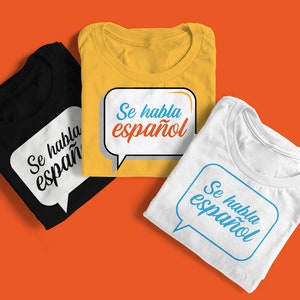 May include: Three folded t-shirts with the text "Se habla español" in a speech bubble. The shirts are black, yellow, and white.
