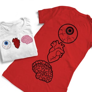Puede incluir: Dos camisetas con ilustraciones anatómicas en blanco y negro de un ojo, un corazón y un cerebro. Las camisetas son rojas y blancas.