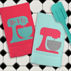 May include: Two kitchen towels with a red and blue stand mixer design. One towel has the text "Mix It Up" on it. A teal spatula is also in the image.