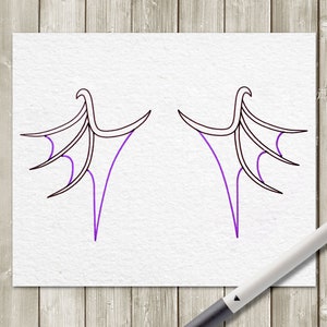 May include: Two symmetrical wing designs drawn in black ink with purple accents on white paper. The wings have a stylized, curved shape with pointed tips and a series of lines suggesting feathers. A pen rests on the wooden surface.