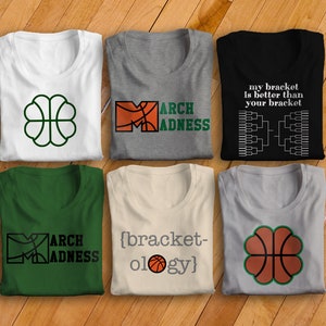 May include: Six folded t-shirts with different designs related to basketball and March Madness. The designs include a basketball in a clover shape, the words "March Madness" with a basketball in the letter M, a bracket, and the text "my bracket is better than your bracket" with a bracket graphic.