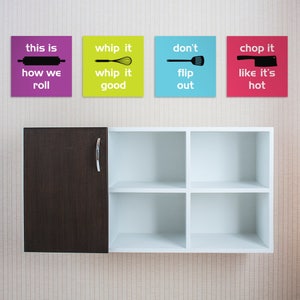 Puede incluir: Cuatro impresiones enmarcadas con refranes y iconos de cocina cuelgan de una pared sobre un armario blanco con una puerta marrón. Las impresiones dicen "this is how we roll", "whip it whip it good", "don't flip out", y "chop it like it's hot".