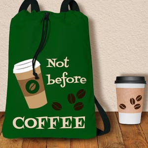 Puede incluir: Una mochila con cordón verde oscuro con las palabras "Not before COFFEE" en blanco. La mochila presenta un gráfico de taza de café e ilustraciones de granos de café. A la derecha hay una taza de café desechable con gráficos de granos de café.
