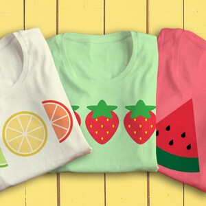 May include: Three white t-shirts with different fruit designs. The first shirt has a lime, lemon, and orange. The second shirt has two strawberries. The third shirt has a watermelon.