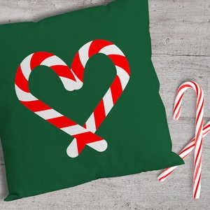 May include: A green throw pillow with a red and white candy cane heart design. Two red and white candy canes are on a white wooden surface.