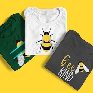 Puede incluir: Tres camisetas dobladas con diseños de abejas. La primera camiseta es verde con un gráfico de abeja y dos líneas azules. La segunda camiseta es blanca con un gráfico de abeja. La tercera camiseta es gris con el texto "bee kind" y un gráfico de abeja.