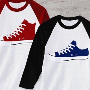 May include: Two baseball style shirts with a red and blue sneaker graphic on the front. The shirts are white with black sleeves.