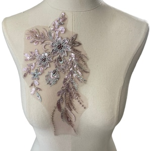 May include: A delicate floral applique with pink, green, and brown sequins and beads on a sheer mesh fabric. The applique features a large flower with smaller flowers and leaves surrounding it.