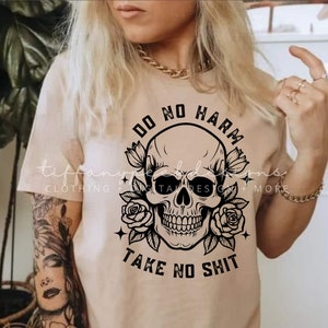 Może przedstawiać: Beżowa koszulka z czarnym nadrukiem czaszki i tekstem "Do No Harm Take No Shit".