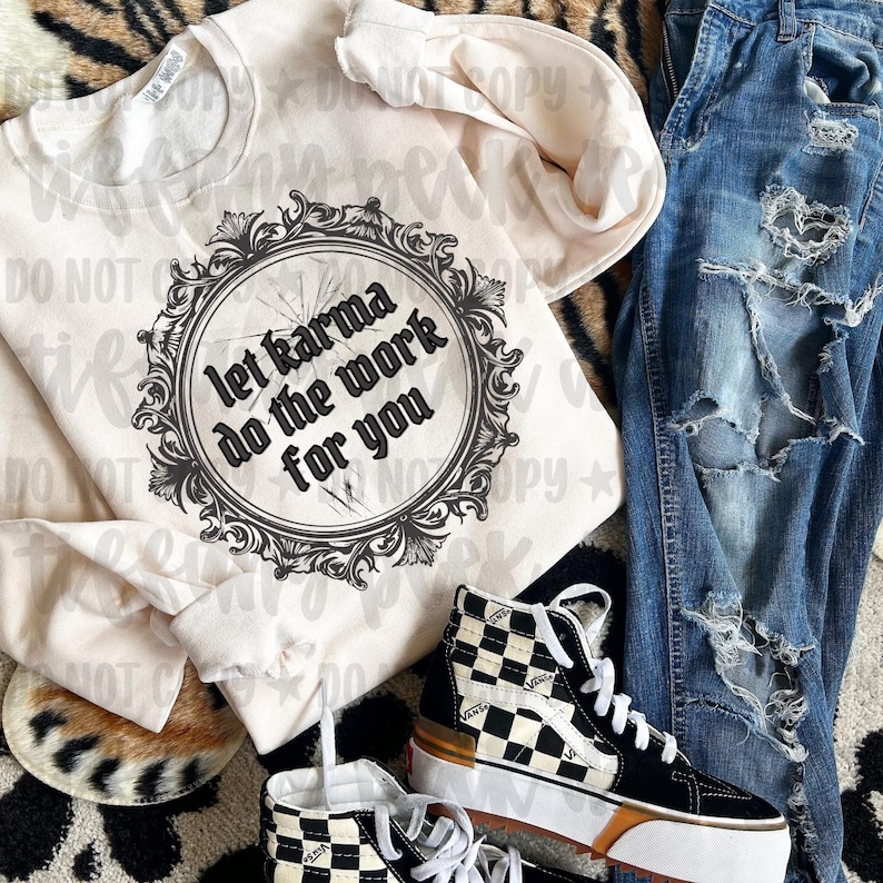 May include: A cream-colored crewneck sweatshirt featuring a black circular ornate frame graphic with the text let karma do the work for you, paired with distressed blue denim jeans and black and white checkered high-top sneakers.