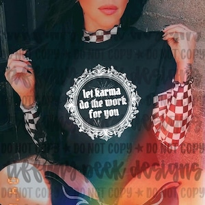 May include: A black short-sleeved t-shirt featuring a white ornate circular frame with the text "let karma do the work for you" in the center. The shirt is worn over a long-sleeved top with a black and white checkered pattern on the sleeves.