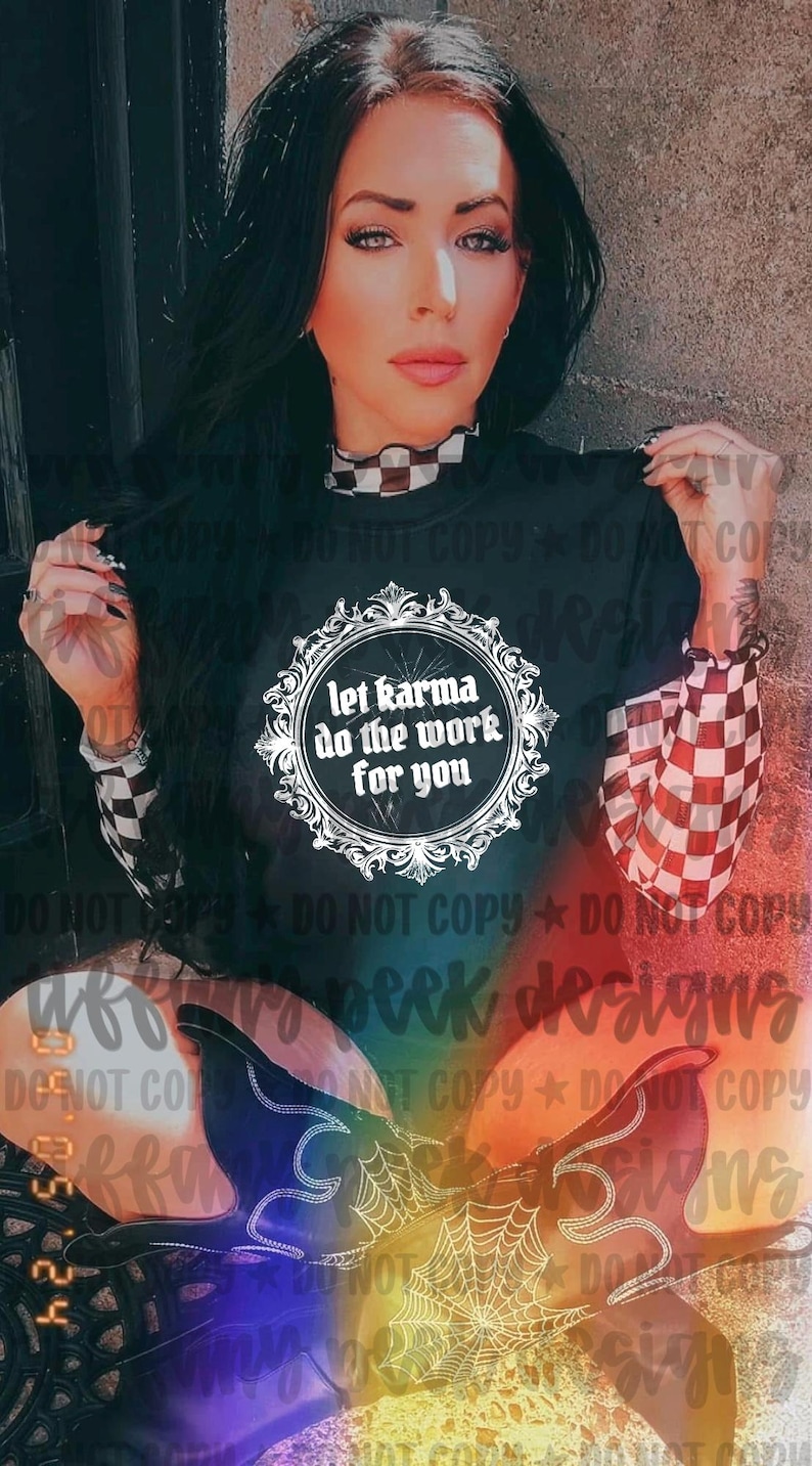May include: A black short-sleeved t-shirt featuring a white ornate circular frame with the text "let karma do the work for you" in the center. The shirt is worn over a long-sleeved top with a black and white checkered pattern on the sleeves.