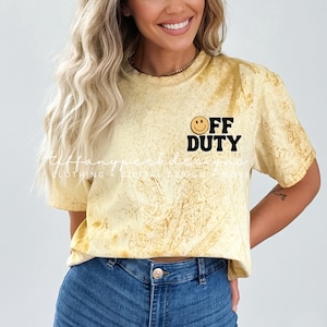 Puede incluir: Una camiseta amarilla tie-dye con una carita sonriente negra y el texto "OFF DUTY" en negro.