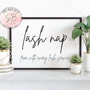 Puede incluir: Una impresión enmarcada en negro con fondo blanco y texto negro que dice "lash nap free with every lash service". La impresión está sobre una superficie de mármol blanco con dos plantas en macetas.