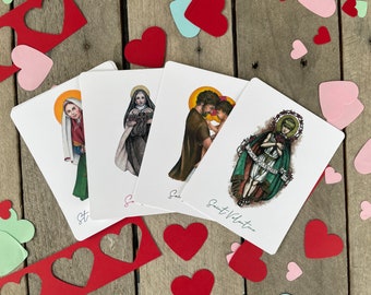 May include: Four white cards featuring illustrations of saints, including Saint Valentine, Saint Agnes, Saint Catherine, and Saint Lucy. The cards are surrounded by red and pink hearts on a wooden background.