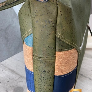 May include: A green cork handbag with blue and brown accents. The bag has a zipper closure and a top handle.