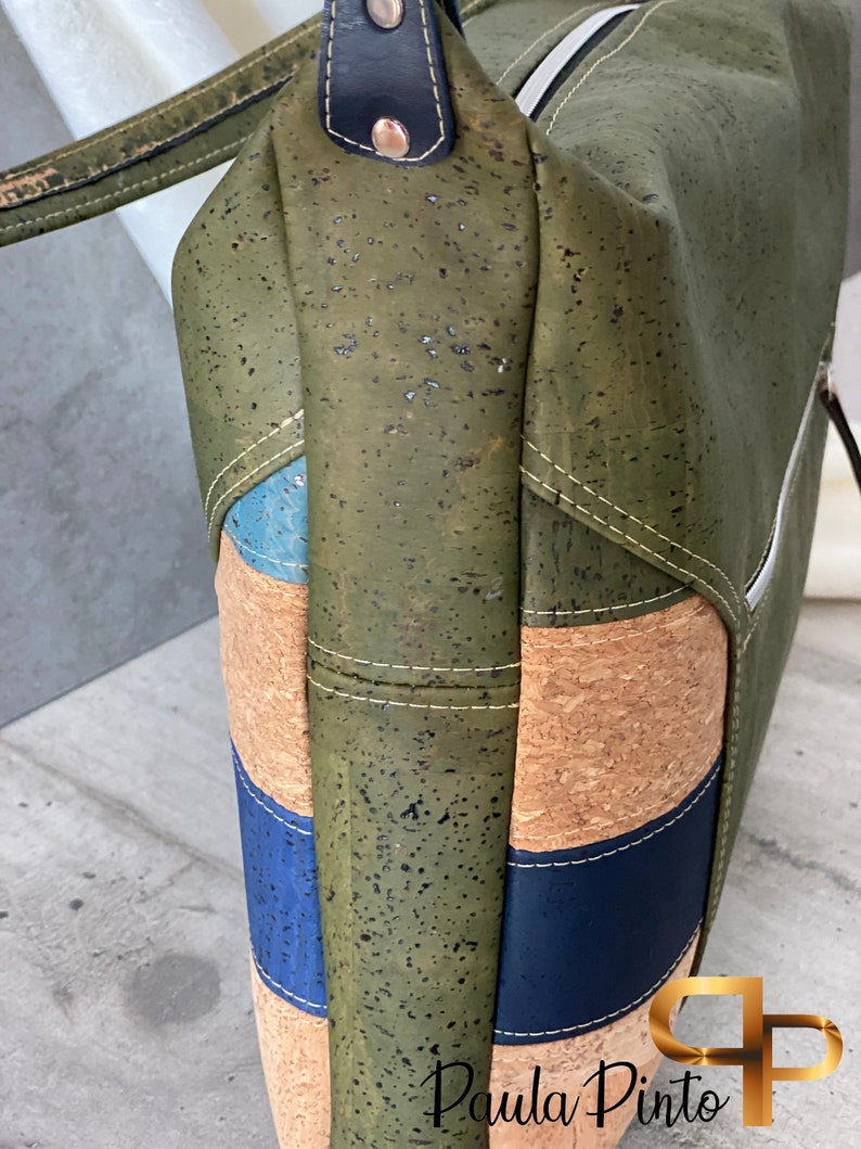 May include: A green cork handbag with blue and brown accents. The bag has a zipper closure and a top handle.