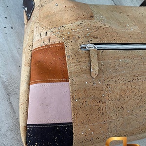 May include: A cork handbag with a zipped pocket and a patchwork design featuring brown, pink, and black fabric. The bag has a gold logo that says "Paula Pinto".