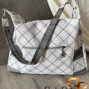 May include: A white and grey plaid tote bag with a grey zippered pocket and a silver charm. The bag has a long grey strap and a silver buckle.
