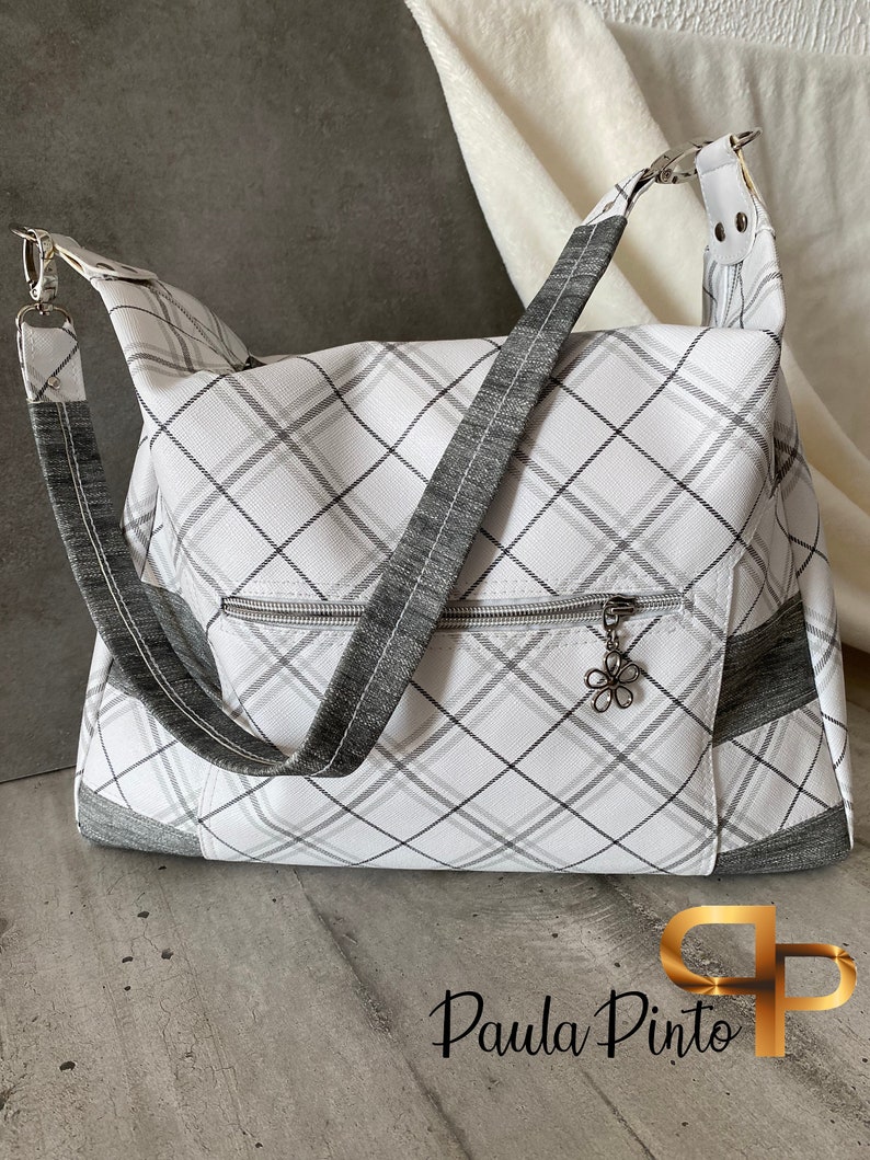 May include: A white and grey plaid tote bag with a grey zippered pocket and a silver charm. The bag has a long grey strap and a silver buckle.
