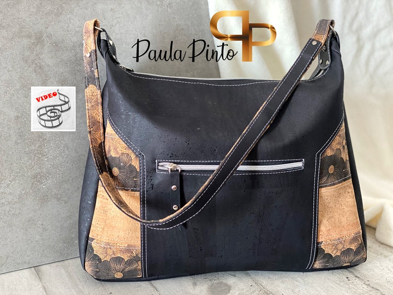 May include: Black cork and brown floral patterned shoulder bag with a zippered pocket and a long adjustable strap. Paula Pinto is written on the bag.