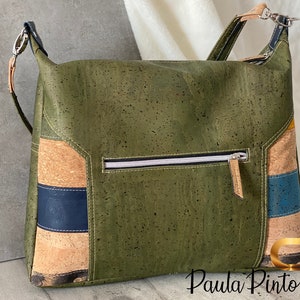 May include: A green cork handbag with a zipped pocket and a brown leather strap. The bag has a patchwork design with brown, blue and yellow accents. The text "Paula Pinto" is visible on the bottom right corner of the bag.