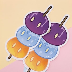 May include: A collection of stickers featuring stylized dango, a Japanese sweet treat. Each sticker shows three colorful, round mochi balls on a skewer. The top ball is purple, the middle is blue, and the bottom is orange.