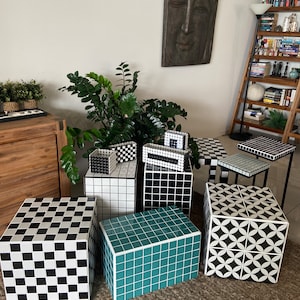 May include: A set of six black and white tiled cube stools with geometric patterns. The stools are arranged in a row on a brown rug.