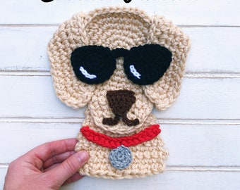 Puede incluir: Patrón de crochet para un perro con gafas de sol, un collar rojo y una etiqueta plateada. El perro está hecho de hilo beige.