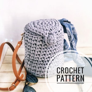 May include: A gray crocheted bag with a brown leather strap. The bag has a round shape and a textured surface. The text "CROCHET PATTERN" is visible in the image.