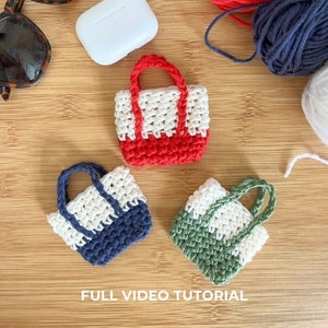 May include: Three miniature crocheted tote bags in different colours. The bags are white with a red, blue, and green bottom. The bags are small enough to fit in the palm of your hand.