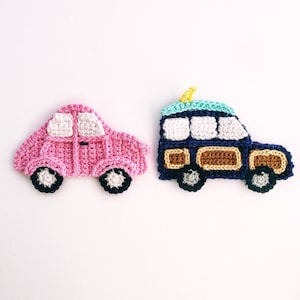Puede incluir: Dos coches de juguete de crochet, uno rosa y otro azul, con detalles blancos y negros. El coche azul tiene una tabla de surf amarilla en la parte superior.