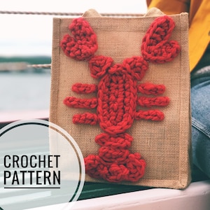 May include: A red crocheted lobster design on a brown burlap tote bag. The bag has the words "CROCHET PATTERN" written on a white circle.