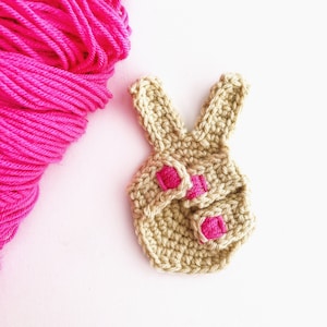 May include: A crocheted bunny outfit in beige with pink accents. The outfit is made with a soft yarn and is perfect for a baby or toddler.