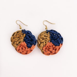 May include: A pair of handmade earrings with a circular design. The earrings are made of woven straw in shades of brown, orange, and blue.