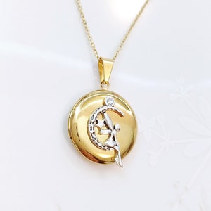 Può includere: Collana con ciondolo in oro a forma di luna crescente e una fata. La fata è realizzata in metallo bianco e ha un piccolo diamante al centro della luna.