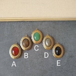 Può includere: Cinque ciondoli a forma di medaglione ovale in oro con pietre di diversi colori. Le pietre sono rosse, marroni, verdi, grigie e nere. I ciondoli sono etichettati dalla A alla E.