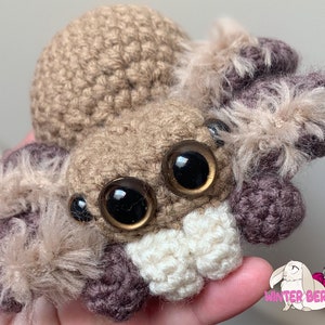 May include: A crocheted brown and purple spider with large black eyes and fluffy brown legs.