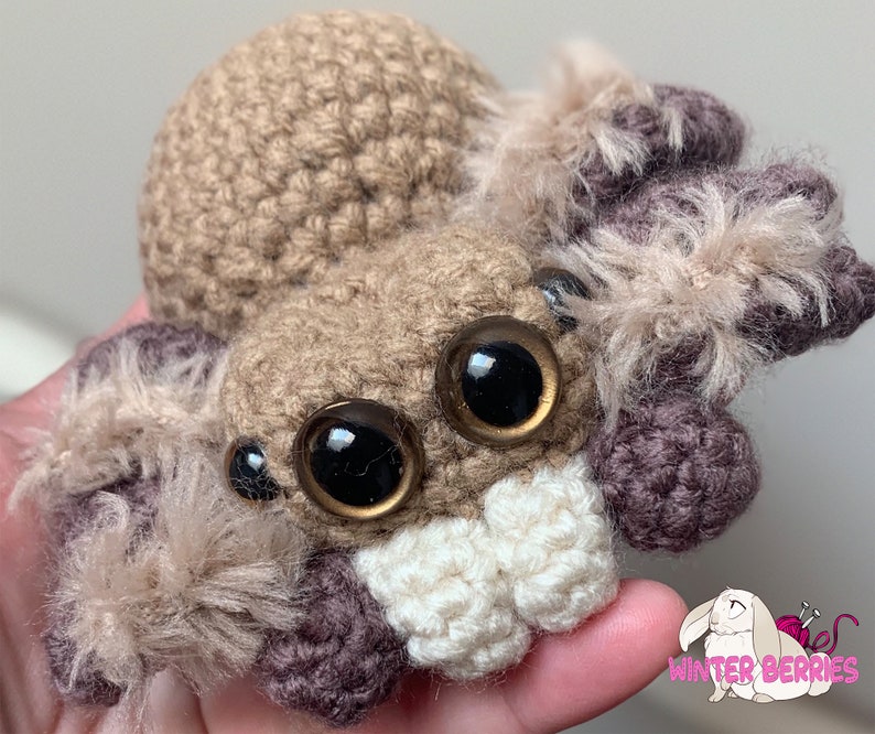May include: A crocheted brown and purple spider with large black eyes and fluffy brown legs.