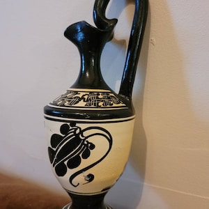 Puede incluir: Jarrón de cerámica blanco y negro con un diseño floral. El jarrón tiene una base ancha y un cuello estrecho con un asa curva.