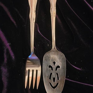 May include: A silver cake server and fork with ornate handles. The server has a decorative cut-out design.