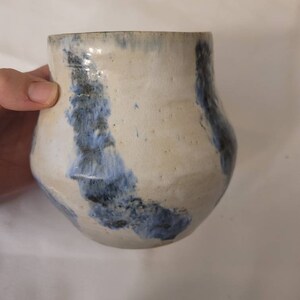 May include: A white ceramic vase with blue and black abstract designs. The vase has a rounded body and a slightly flared opening.