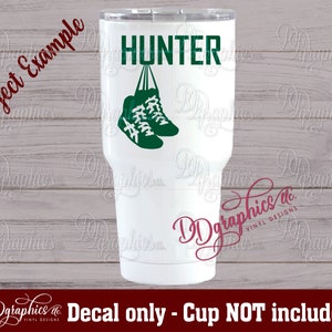 Op de afbeelding: Een witte tumbler met een groene en zwarte sticker van een paar sneakers die aan het woord "HUNTER" hangen.