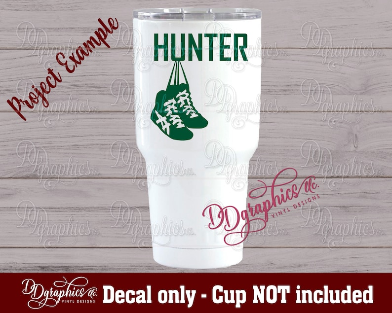 Op de afbeelding: Een witte tumbler met een groene en zwarte sticker van een paar sneakers die aan het woord "HUNTER" hangen.