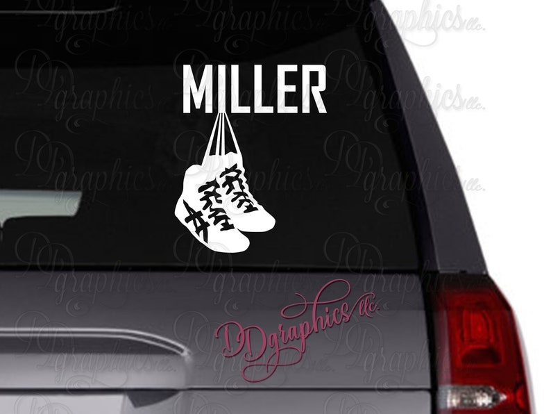 Op de afbeelding: Witte vinyl sticker met het woord "MILLER" en twee witte sneakers die aan de letters hangen. De sneakers zijn aan elkaar gebonden met een touwtje.