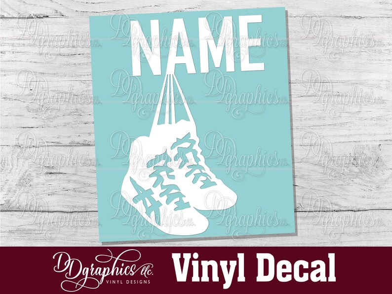 Op de afbeelding: Witte vinyl sticker van een paar sneakers die aan het woord "NAME" hangen op een lichtblauwe achtergrond.