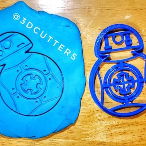 May include: A blue plastic cookie cutter shaped like the Star Wars character BB-8. The cutter is shown on a blue background with the text "@3DCUTTERS" in white.