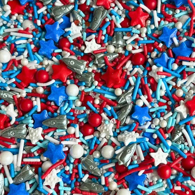 Macro close up of a buttercream frosting swirl decorated with metallic silver rocket ship sprinkles and red and blue stars. Luxury Birthday Sprinkles Custom Sprinkles Cake Sprinkles Cupcake Décor Rocket Birthday Décor Space Sprinkles