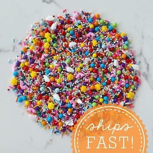 Puede incluir: Una colorida variedad de chispas, que incluye formas de estrella, nube y animal, y pequeñas chispas redondas y en forma de palito. Las chispas son de varios colores, como rojo, amarillo, azul y rosa. El texto "ships FAST!" está en un círculo naranja.