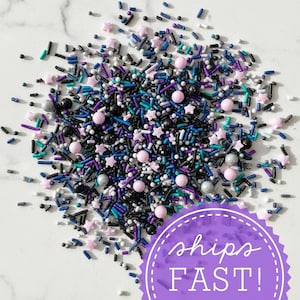 May include: A colorful mix of sprinkles, including star-shaped, round, and rod-shaped pieces in shades of black, purple, blue, pink, and silver. The sprinkles are scattered on a white surface. The image includes the text "ships FAST!"